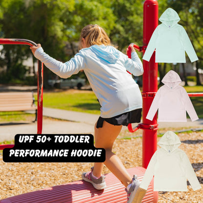 A young girl in a white performance hoodie is climbing on a red bench in a park, with a red pole and a red bench visible in the background.