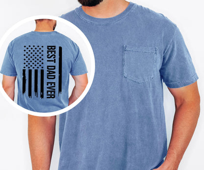 May include: A blue short-sleeved t-shirt with a chest pocket. The back of the shirt features a black graphic of the American flag with the text "BEST DAD EVER" printed vertically on the right side.