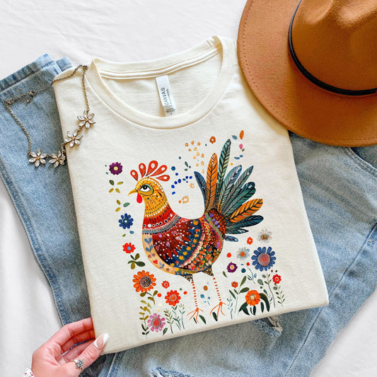 a white t-shirt with a colorful, floral-designed rooster printed on it, along with a brown hat and some jewelry.