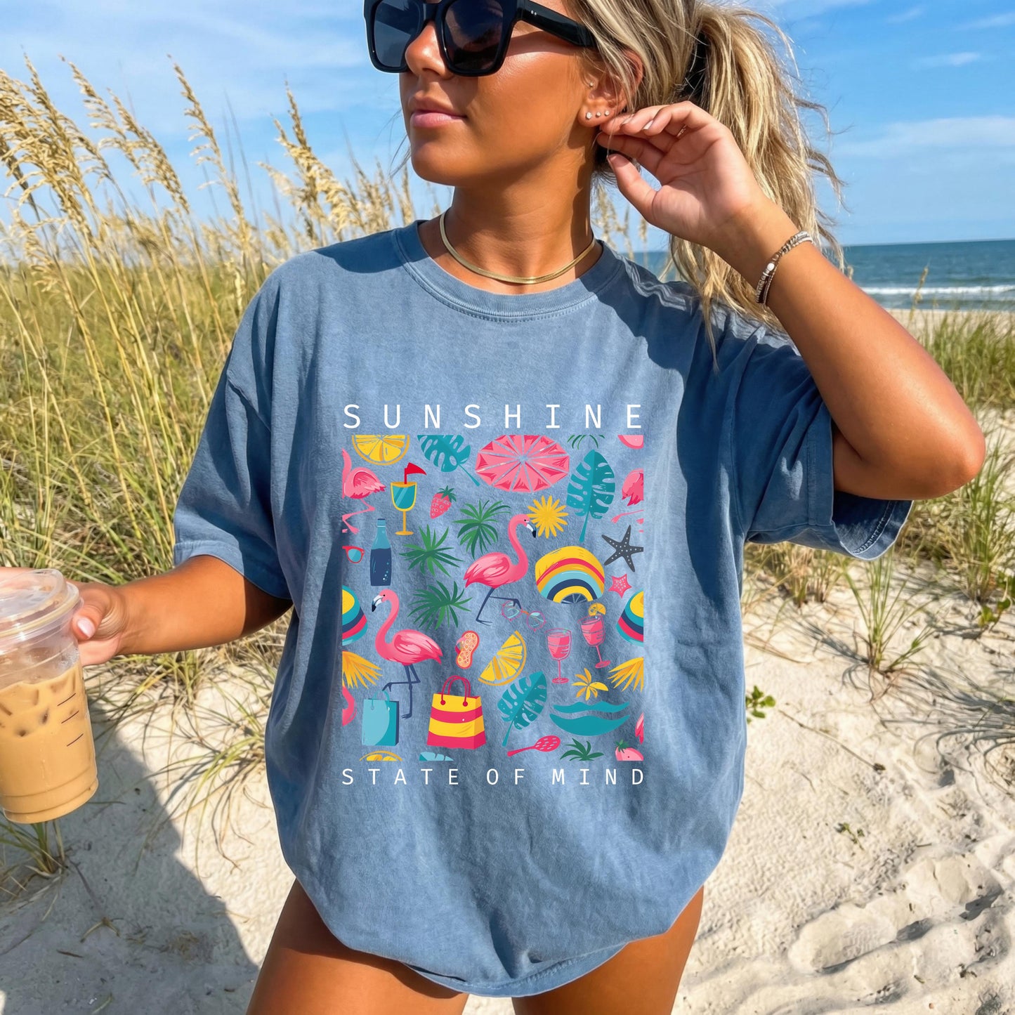 May include: Blue t-shirt with the words "SUNSHINE STATE OF MIND" in white. The shirt features a colorful graphic of flamingos, beach umbrellas, tropical leaves, and other summer-themed illustrations.