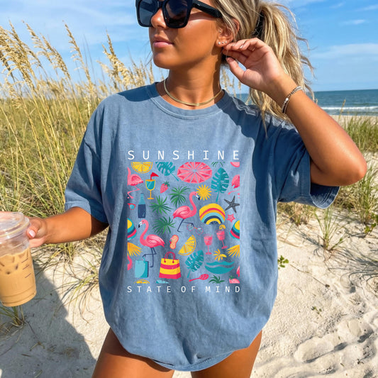 May include: Blue t-shirt with the words "SUNSHINE STATE OF MIND" in white. The shirt features a colorful graphic of flamingos, beach umbrellas, tropical leaves, and other summer-themed illustrations.